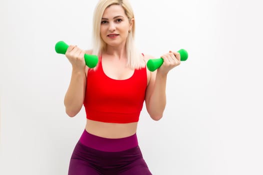 Smiling athletic woman pumping up muscles with dumbbells on white background