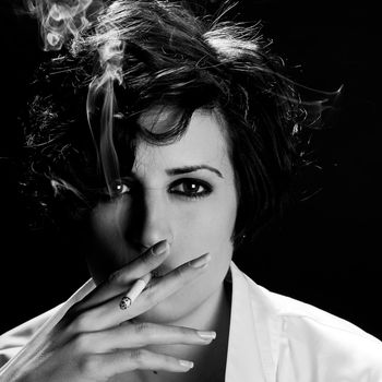 Close-up portrait of a brunette woman smoking a cigarette on black background