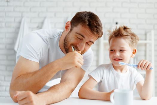 Dad and little son brushing teeth together in bathroom