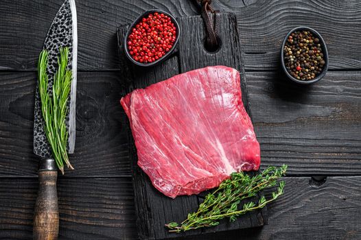 Raw flank or bavette beef meat steak on a wooden cutting board. Black background. Top view.