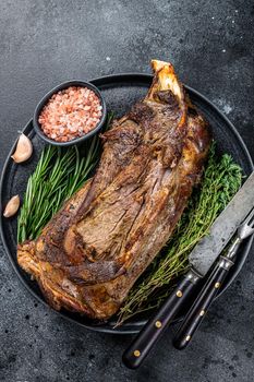 Roasted lamb mutton shoulder meat on a plate with knife and fork. Black background. Top view.