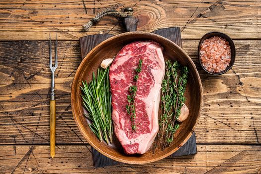 Fresh new york strip beef meat steak or striploin in a wooden plate with herbs. wooden background. Top view.