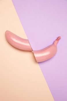 From above of halved unpeeled banana painted in pink color arranged on two color background