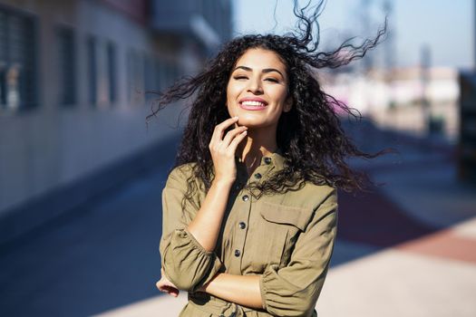 Arab woman with curly hair moved by the wind in urban background