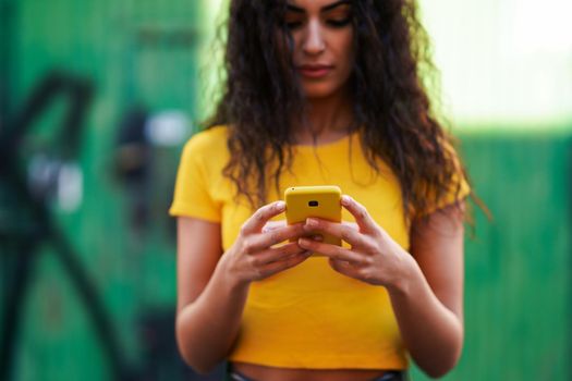 Young Arab woman texting a text message with her smartphone against green urban wall.