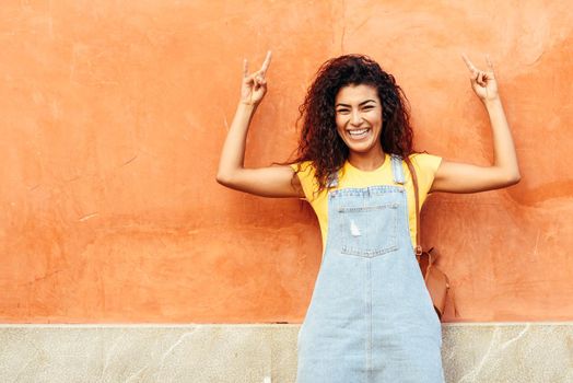 Funny black woman with black curly hairstyle outdoors. Arab girl in casual clothes in the street. Happy female wearing yellow t-shirt and denim dress in urban background.