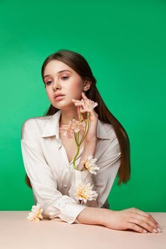 Crop female model with fresh flowers growing from blouse sleeves touching face against green background