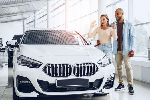 Young happy couple choosing a new car in car dealership