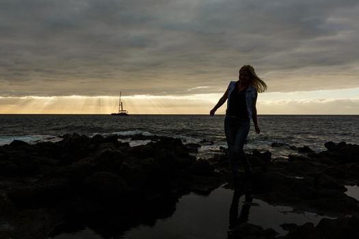 Women on volcanic rocks and blue ocean with waves, white foam and volcanic rocks. Canary Islands. The magnificent coast of the Atlantic Ocean.