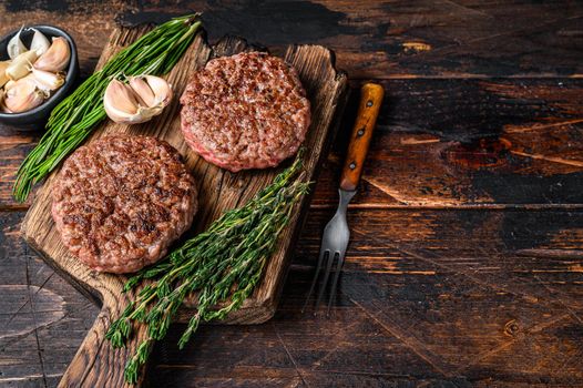 Barbecue steak patties for burger from ground beef meat on a wooden cutting board. Dark wooden background. Top view. Copy space.