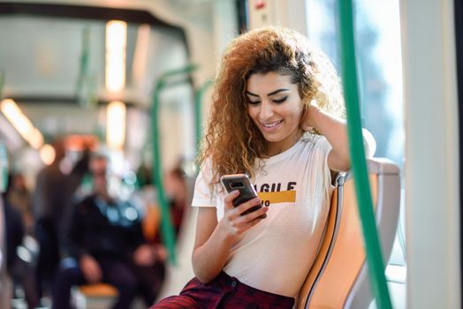 Arabic woman inside subway train looking at her smart phone. Arab girl in casual clothes.