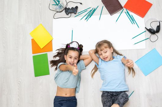 family, leisure and childhood concept - happy sisters lying on floor and drawing and doing homework at home