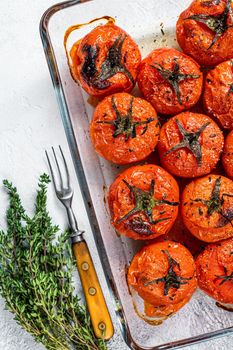 Roasted tomatoes with olive oil and thyme in baking dish. White background. Top view.