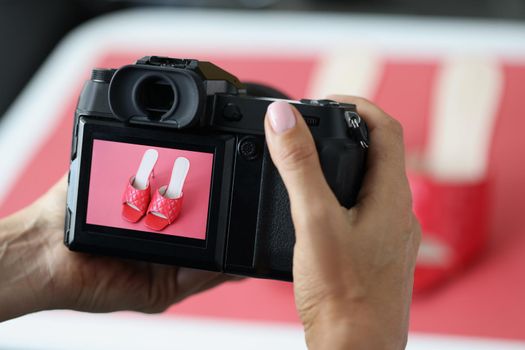 Close-up of woman professional photographer taking picture of red trendy shoes. Creating picture for advertisement. Fashion photographer, promotion concept