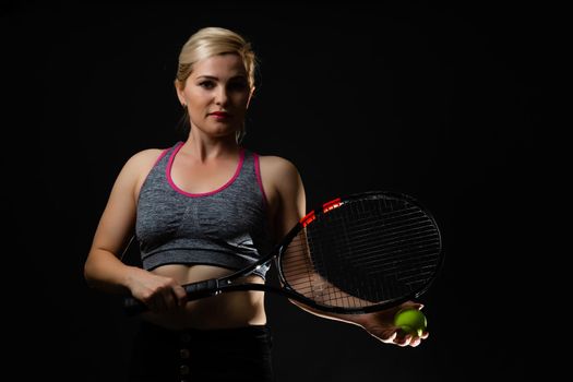 Young female tennis player posing with racket on black background