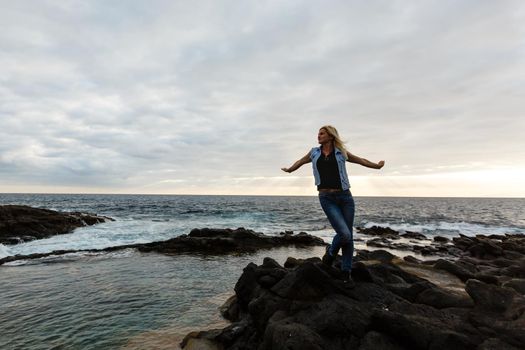 Women on volcanic rocks and blue ocean with waves, white foam and volcanic rocks. Canary Islands. The magnificent coast of the Atlantic Ocean.