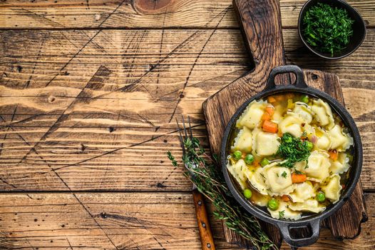 Broth soup with ravioli dumplings pasta in a pan. Wooden background. Top view. Copy space.