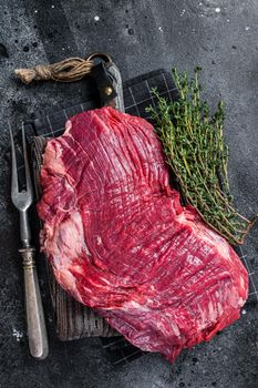 Uncooked Raw Flank or flap beef steak on butcher board. Black background. Top view.