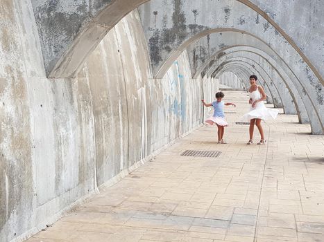 Funny mother and daughter dancing under the arches of the Port of Malaga in Andalusia, Spain. Females wearing dress.