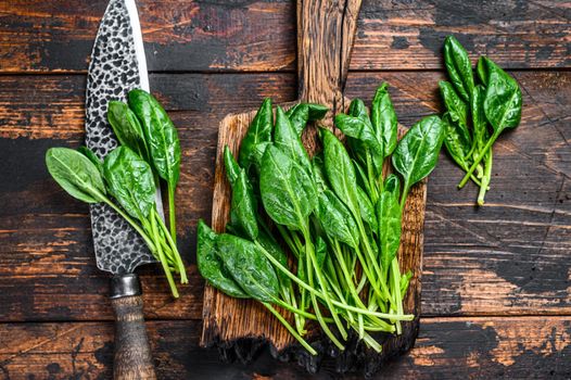 Young baby spinach leaves on a wooden cutting board. Dark wooden background. Top view.