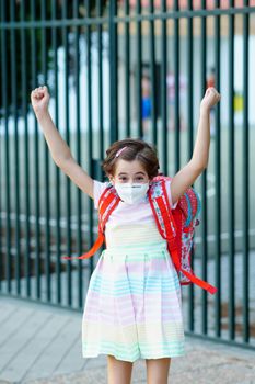 Girl wearing a mask takes a jump for joy at going back to school. Back to school concept.
