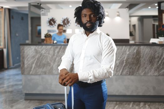 Black businessman with packed luggage standing in hotel lobby close up