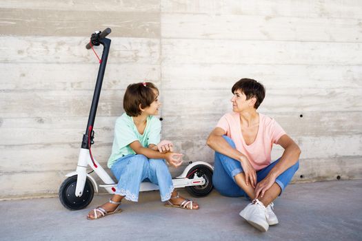 Mother and daughter laughing sitting on an electric scooter in the city street