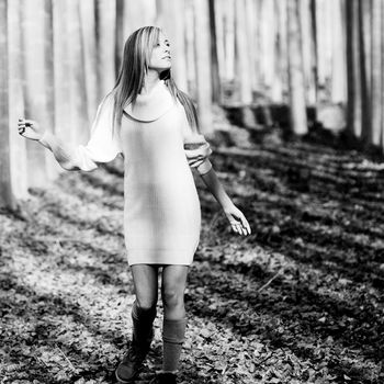 Beautiful blonde girl, dressed with a beige dress, standing in a poplar forest