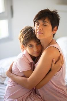 Beautiful young woman and her charming little daughter are hugging on the bed.