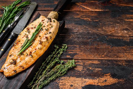 Baked trout fillet on a cutting board. Dark wooden background. Top view. Copy space.