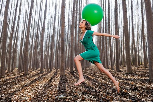 Beautiful blonde girl, dressed in green, jumping into the woods with a balloon in Fuente Vaqueros, Granada, Spain