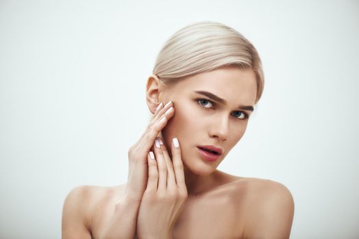 Natural beauty. Portrait of gorgeous blonde woman touching her perfect soft skin while standing against grey background. Skin care. Cosmetics concept