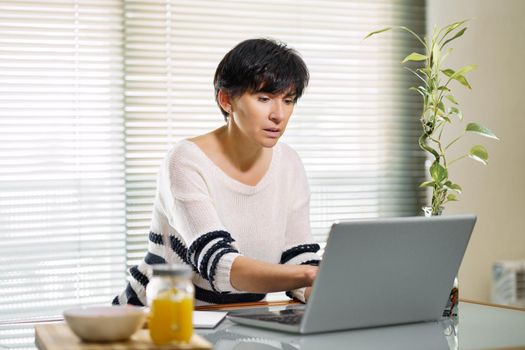 Woman teleworking from home with her laptop. Female in her 50s