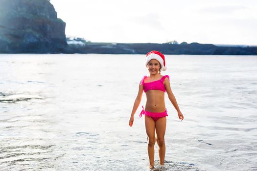 Little cute girl in red hat santa claus on the beach