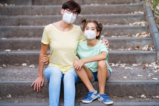 Middle-aged mother and daughter sit on the street wearing masks because of the Covid-19 pandemic