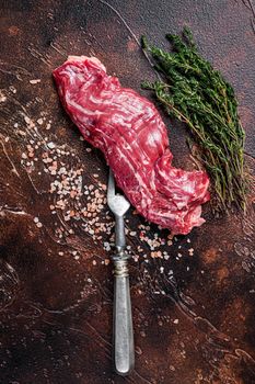 Raw machete skirt beef steak on meat fork. Dark background. Top view.