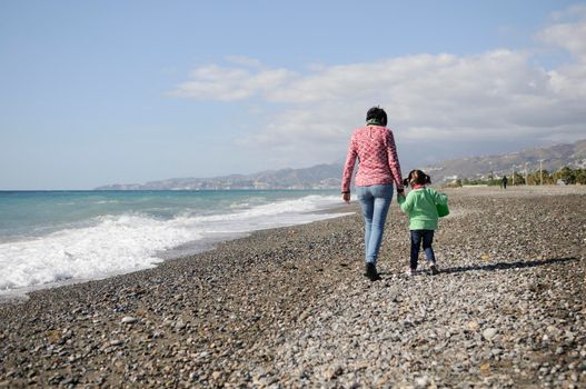 Mother and little daughter having fun on the beach in winter