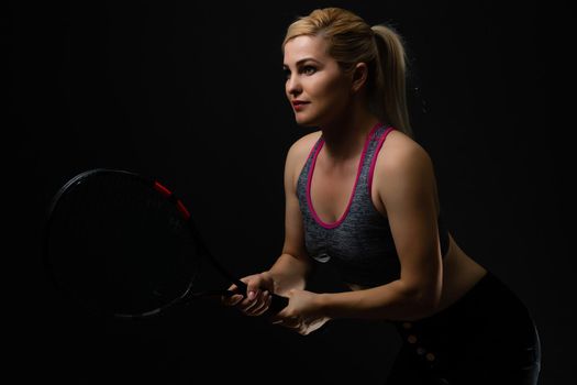 Young female tennis player posing with racket on black background