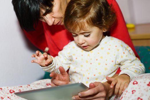 Mother reading bedtime stories to her little daughter on digital tablet