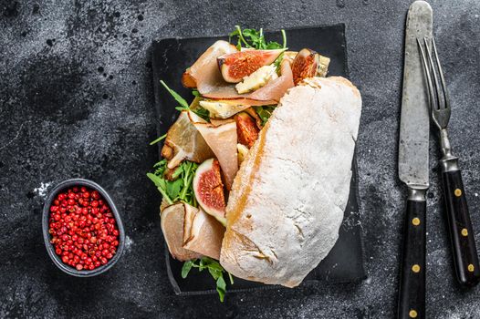 Sandwich with baguette, ham, fig, arugula and prosciutto meat. Black background. Top view.