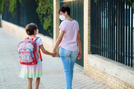 Nine years old girl with bag walking with her mother hand in hand wearing masks. Back to school concept.