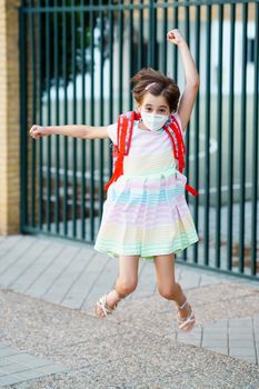 Girl wearing a mask takes a jump for joy at going back to school. Back to school concept.