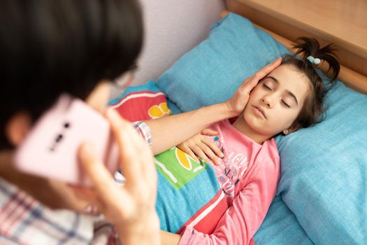 Mother worried about her daughter's temperature calling the doctor. Little girl on bed.
