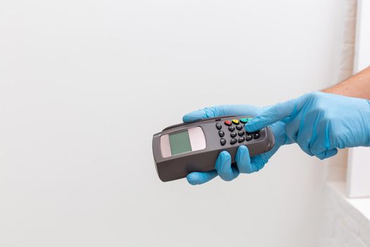 Cashier hand holding credit card reader machine and wearing disposable gloves, paying with smartphone during Covid-19 pandemic.