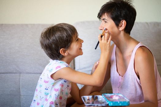 Happy beautiful mother and her little cute daughter doing make up for each other. Mum spending free time with her daughter.