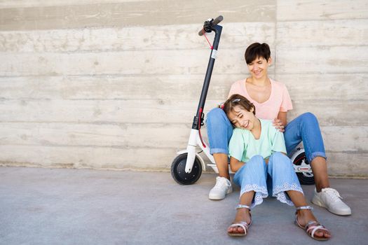 Mother and daughter laughing sitting on an electric scooter in the city street