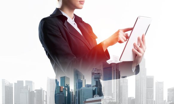 Young businesswoman using tablet computer. Double exposure concept with modern cityscape and beautiful woman in business suit. Digital technology in property management and development company.