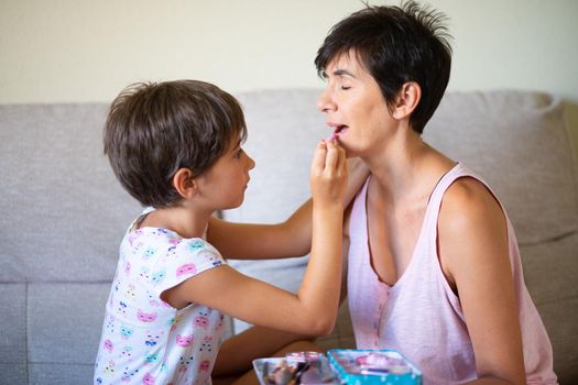 Happy beautiful mother and her little cute daughter doing make up for each other. Mum spending free time with her daughter.