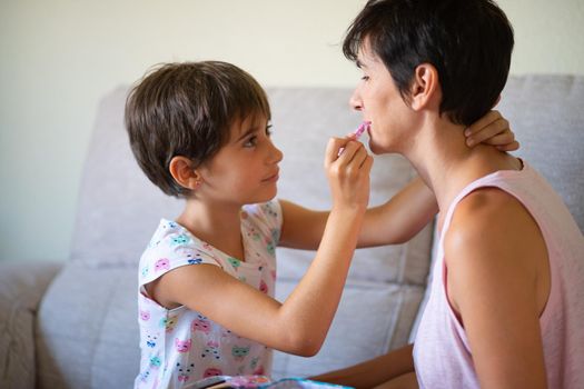 Happy beautiful mother and her little cute daughter doing make up for each other. Mum spending free time with her daughter.