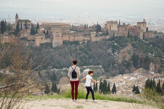 Mother and little daughter looking at the Alhambra of Granada from Cerro de San Miguel. Single parent family doing tourism.
